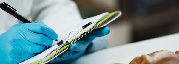 person wearing blue gloves writing on a clipboard with a pen and a brown object in the background related to research 3 important notes