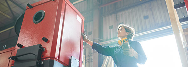 woman inspecting red industrial equipment in warehouse setting for manufacturing processes