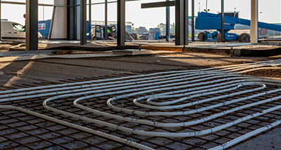 construction site with white tubing laid out on a steel reinforcement grid foreground and unfinished walls in the background indicating plumbing and heating installation process