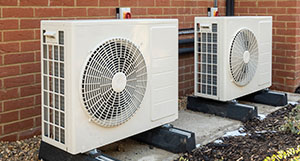 two outdoor air conditioning units next to each other installed on a concrete slab against a brick wall