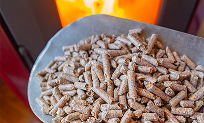 Close-up of a metal scoop filled with wood pellets in front of a warm fireplace ideal for heating and biomass fuel efficient for 11 seasons